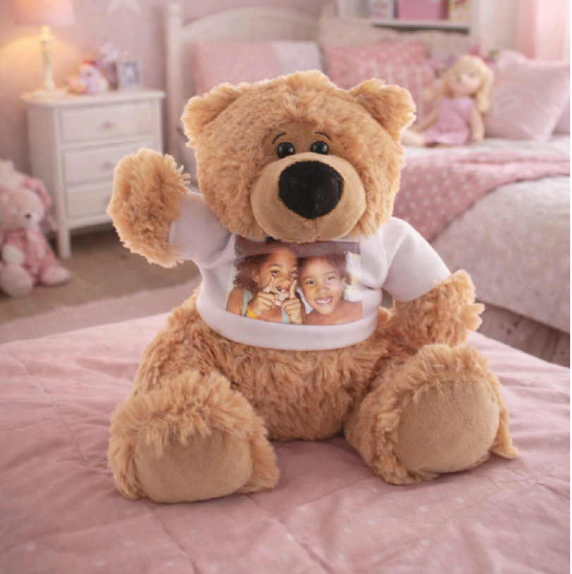 Brown teddy bear wearing a mini shirt printed with a photo of sisters making funny faces.