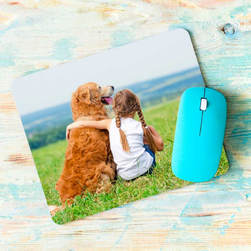 Mousepad printed with a photo of a little girl holding her dog in a grass field outdoors.