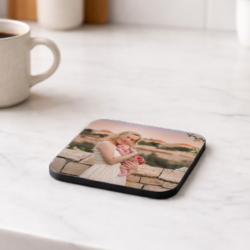 Square coasters printed with a photo of a mother holding her baby beside a wall.
