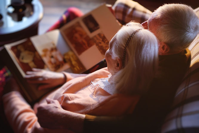 Elderly Couple Looking Through Square Photobook of Memories Elderly couple viewing a square photobook together with personal photos and memories