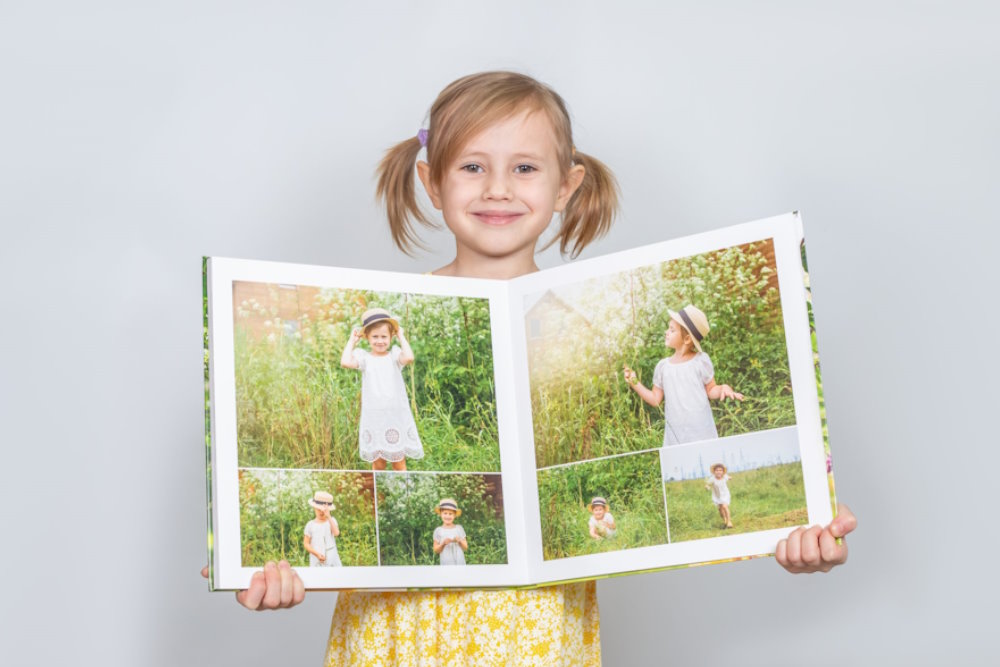 Girl Holding Square Hardcover Photobook Girl holding a square hardcover photobook with printed photo pages displayed inside.