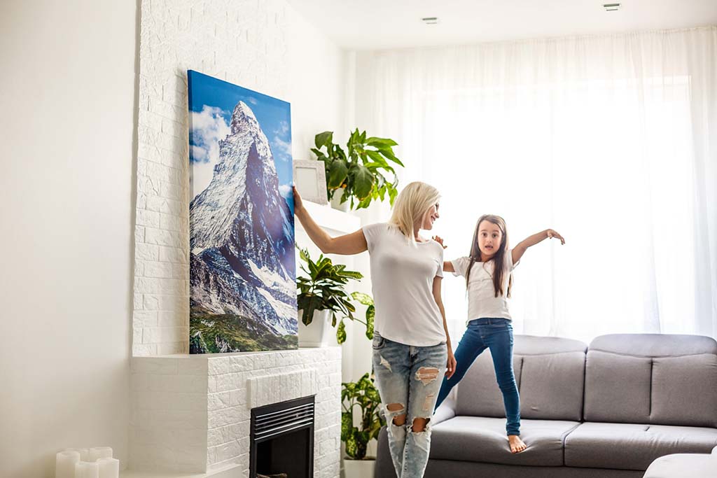 Mother and daughter hanging a canvas photo print on a wall as part of home décor arrangement.